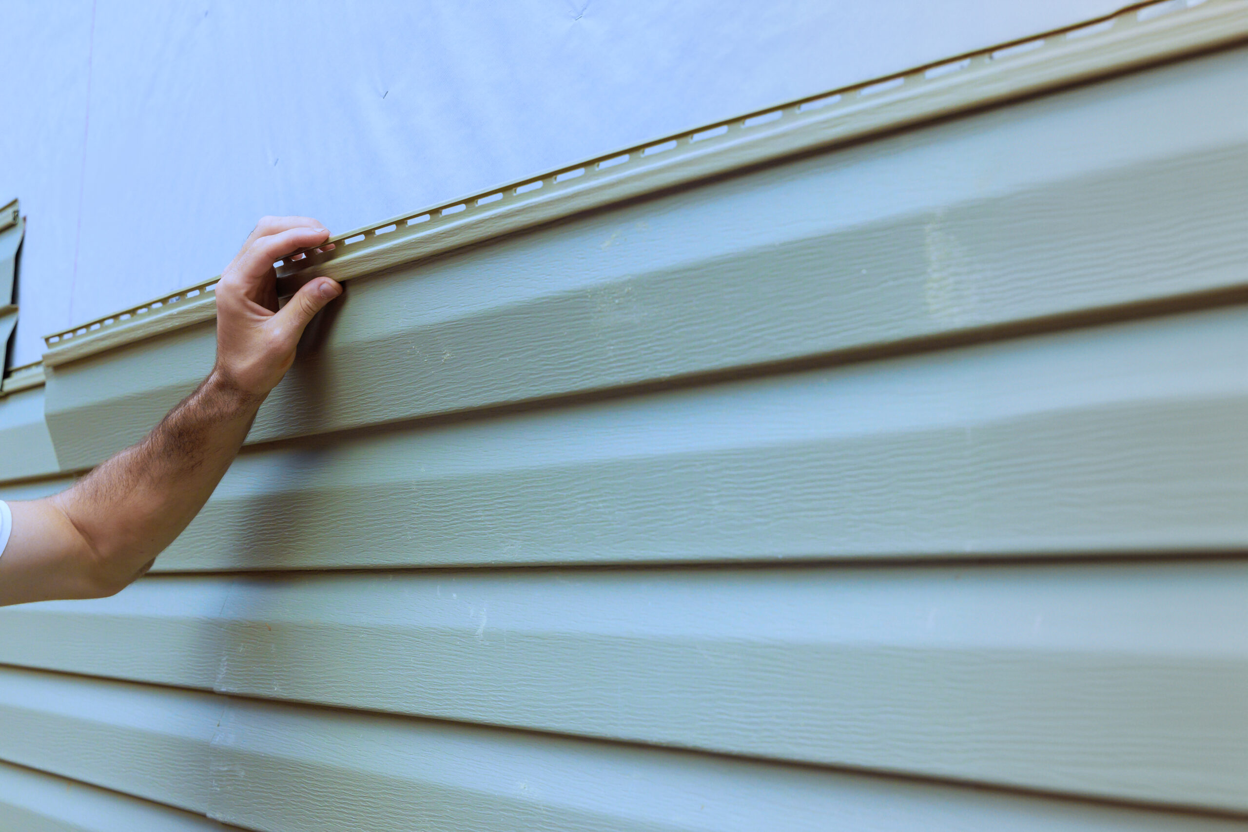 An experienced contractor installs vinyl siding plastic panels on facade wall of new home